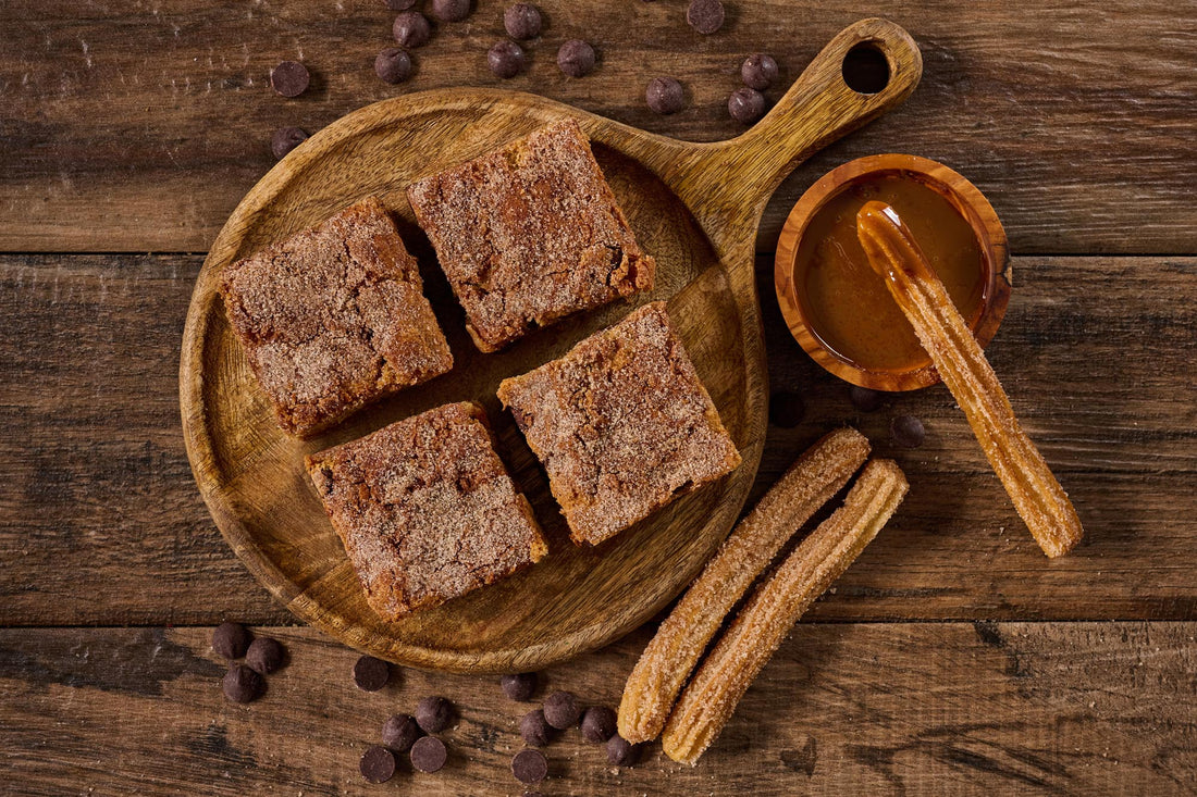 Churro Dulce de Leche Blondie with buttery cinnamon blondie base, swirled with dulce de leche, Ghirardelli dark chocolate chips, and topped with cinnamon sugar for a rich, caramelized treat