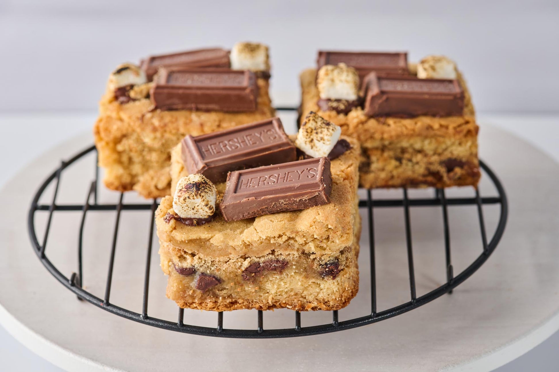 S'mores Blondie with rich buttery base, pockets of melted chocolate and gooey marshmallow, topped with graham cracker crumbs, toasted marshmallows, and Hershey's chocolate for a decadent s'mores treat.